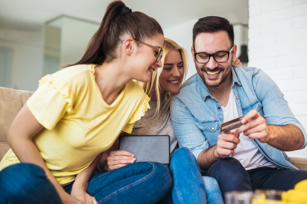 Two women and a man in living room holding credit card and digital tablet, shopping online - Photo, Image