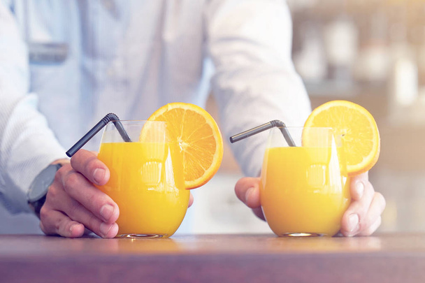 The barman gives two glasses of orange juice to the client of the hotel restaurant. The waiter transfers the order for two orange juice to the client of the hotel bar. The concept of service. Toning - Foto, immagini