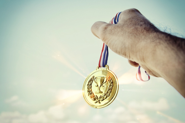 man hand raised, holding gold medal against sky. award and victory concept - Photo, Image
