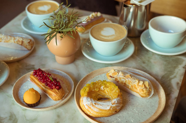 Cafe table with cups of coffee, eclairs and cake - 写真・画像