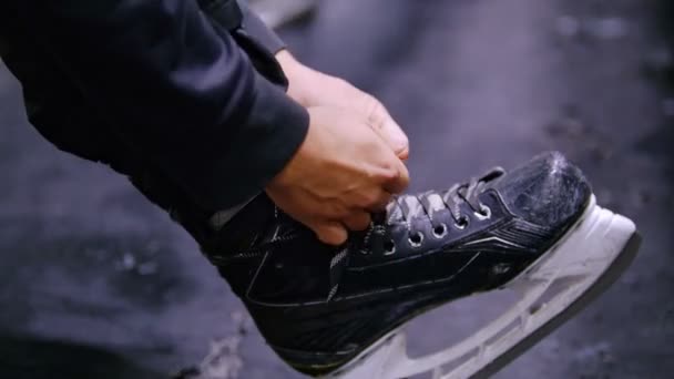 Hands tie shoelaces on hockey skates against the background of the dark floor - Footage, Video