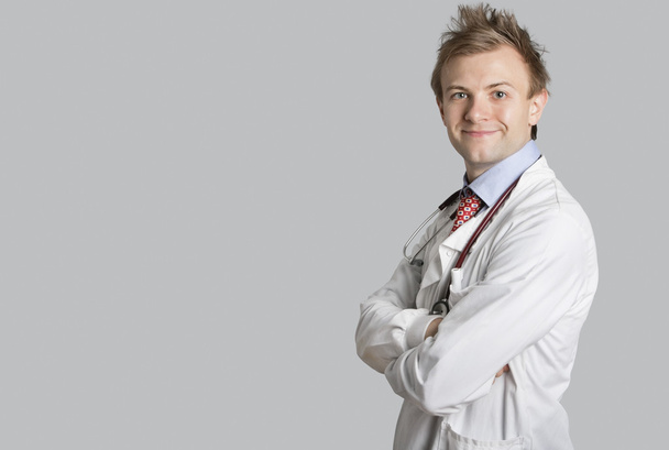 Portrait of a male doctor smiling with arms crossed over gray background - Фото, зображення