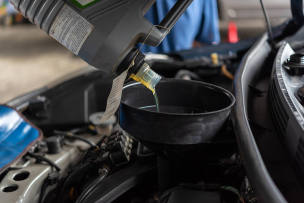 Automekaanikko tai huoltomies täyttää tuoreen voiteluaineen moottoriöljyn autotallissa auton korjausta tai huoltoa varten
 - Valokuva, kuva