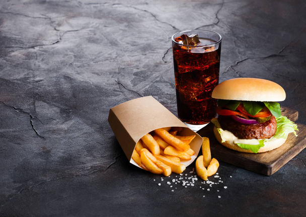 Fresh beef burger with sauce and vegetables and glass of cola soft drink with potato chips fries on stone kitchen background. - Photo, Image