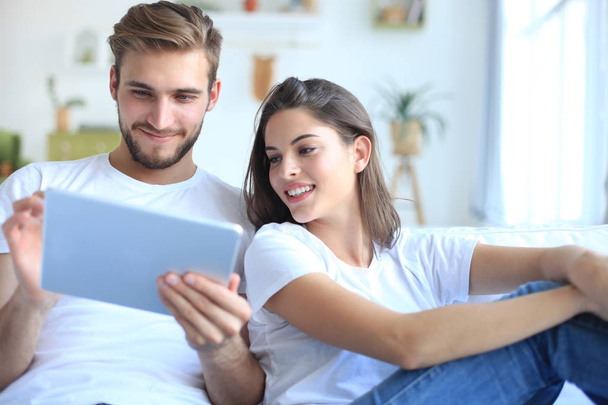 Giovane coppia che guarda contenuti multimediali online in un tablet seduto su un divano in soggiorno. - Foto, immagini