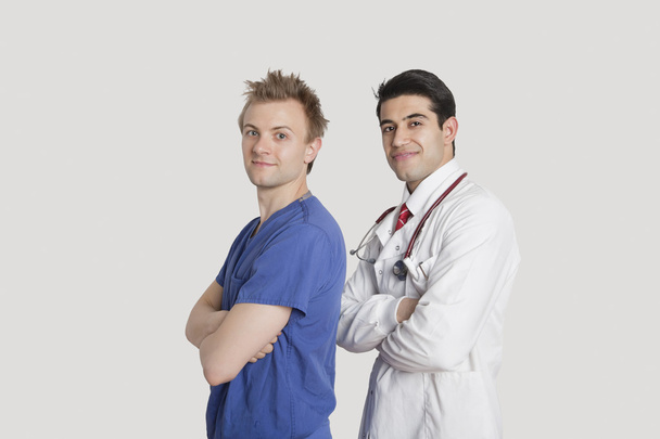 Portrait of a confident doctor and male nurse standing with arms crossed over gray background - Φωτογραφία, εικόνα