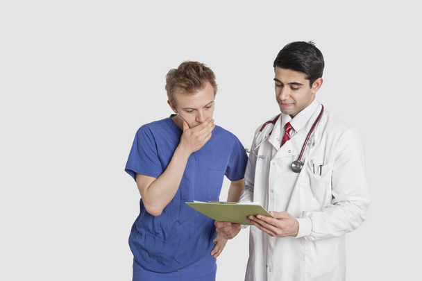Doctor discussing medical report with male nurse over gray background - Φωτογραφία, εικόνα