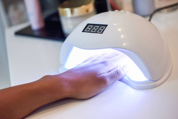 Маникюрные ногти в ультрафиолетовой лампе. Маникюр и маникюр. Руки женщины в салоне велнес
 - Фото, изображение