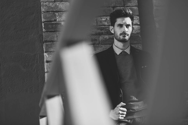 Vonzó az utca emberét brit elegáns ruha viselése. Fiatal szakállas üzletember, a városi háttérben modern frizura. Fekete-fehér fénykép. - Fotó, kép