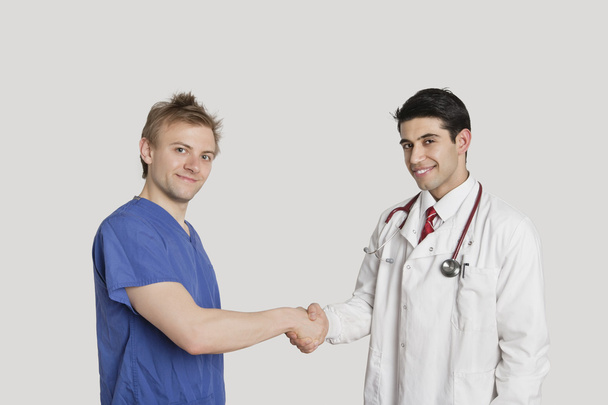 Portrait of doctor and male nurse shaking hands over gray background - Fotoğraf, Görsel
