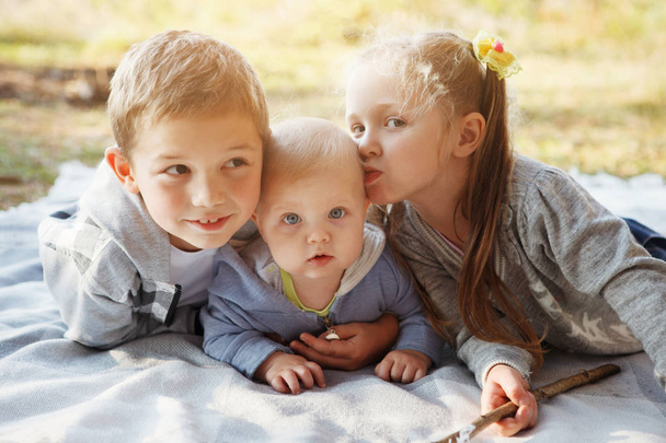 Três crianças, irmão mais velho, irmã loira e menino de 7 meses de idade com olhos azuis estão deitados em um tapete na floresta de outono.
. - Foto, Imagem