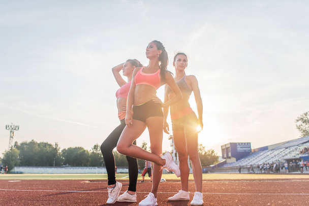 Group of fit young sportswomen standing in athletics stadium and posing. - Photo, Image