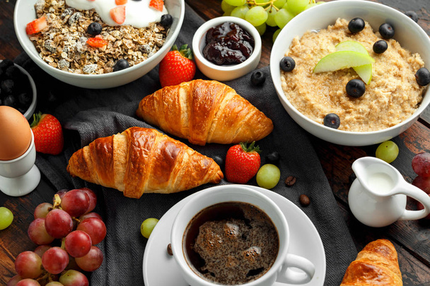 Gezond ontbijt geserveerd met koffie, sinaasappelsap, croissants, ei, granen, havermout en fruit. - Foto, afbeelding