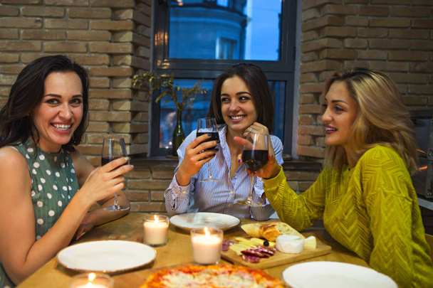 Τρεις φίλες το ψήσιμο με το κόκκινο κρασί στην κουζίνα. Επικεντρωθεί στην μεσαία γυναίκα - Φωτογραφία, εικόνα