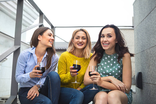 Three young happy woman laughing, drinking red wine, having fun. Party and friendship concept.  - Photo, Image