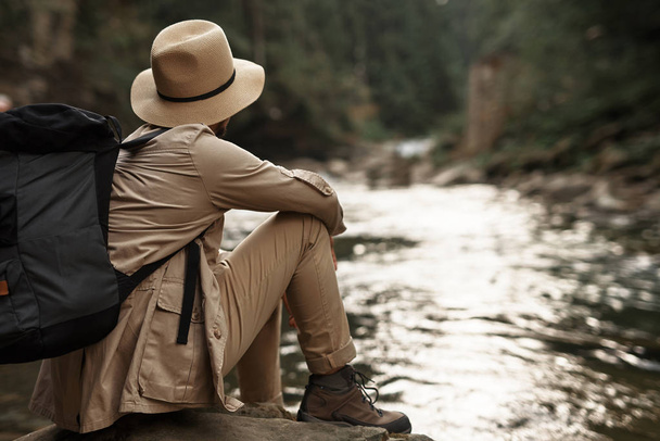 Tired traveler thoughtfully looking at the river while sitting - 写真・画像