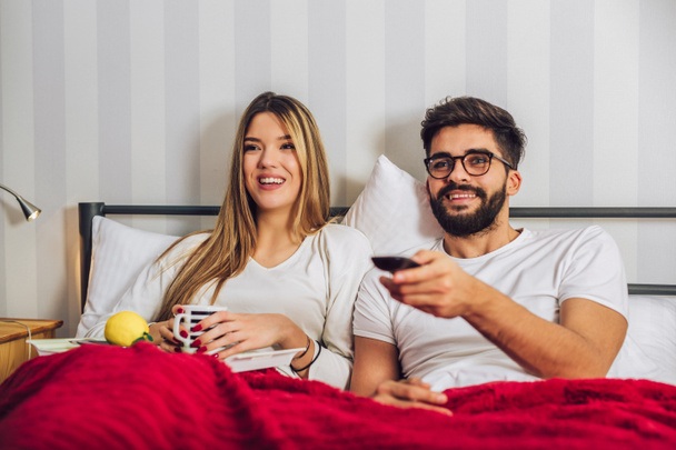 Beautiful young couple watching TV in Bed. - Zdjęcie, obraz