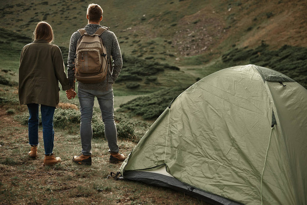 Full length of young travelers holding hands and standing near the tent - Фото, изображение