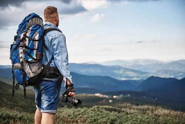 Tall young man carrying heavy backpack and holding his camera - Foto, afbeelding