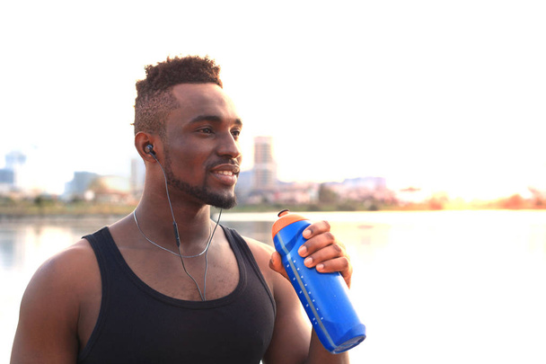 Homme africain en vêtements de sport exercice d'eau potable sur la plage portrait en plein air, au coucher du soleil ou au lever du soleil
. - Photo, image