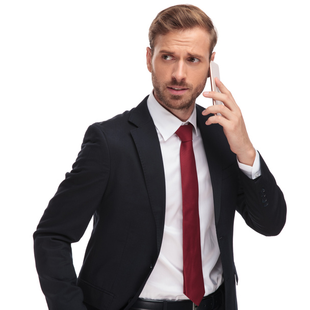 portrait of worried businessman talking on the phone and looking to side while standing on white background - Photo, Image