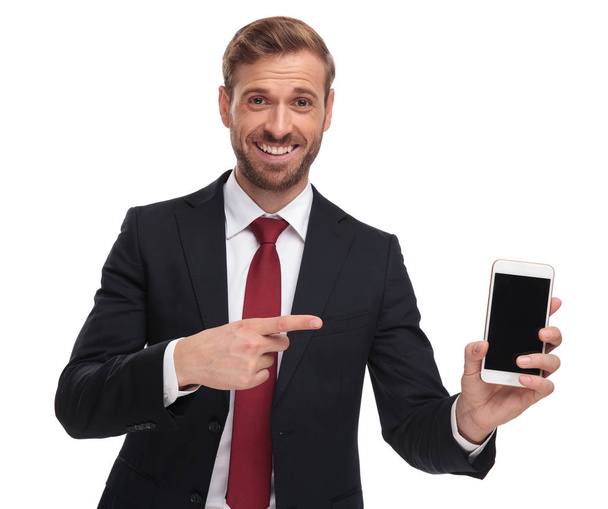 retrato de hombre de negocios feliz apuntando a la pantalla del teléfono móvil mientras está de pie sobre fondo blanco
 - Foto, imagen