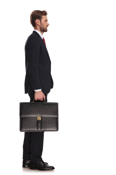 Seitenansicht eines Geschäftsmannes mit Koffer, der in der Schlange steht, während er auf weißem Hintergrund steht, Bild in voller Länge - Foto, Bild