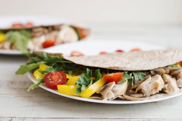 Healthy salad with chicken breast, mushrooms, yellow bell pepper, parsley, arugula and cherry tomatoes in a whole wheat wrap and served on white plate - Zdjęcie, obraz