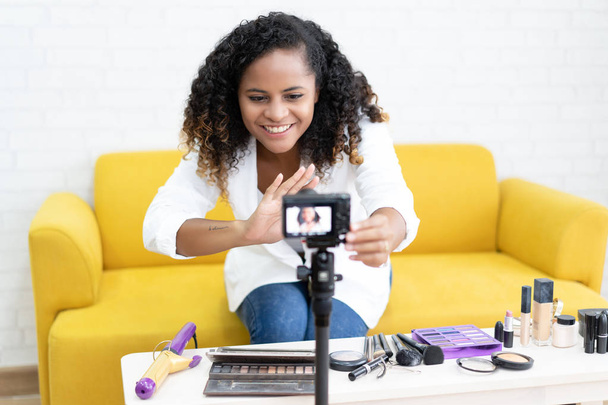 ビデオ記録撮影自宅でビデオブロガー設定カメラを女性黒少女を作る。Web インフルエンサーとして働いて、化粧品のビデオ レビューを記録、ビデオブログを作る若いアフロ アフリカ系アメリカ人の女性。ビデオブログ コンセプト. - 写真・画像