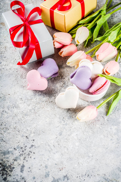 バレンタイン グリーティング カードの休日の背景。バレンタインデーの提示、スウィートの治療します。自家製のパステル カラーのマカロン クッキー、チューリップの花、明るい灰色コンクリート背景にコピー スペース - 写真・画像