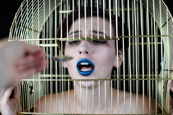 Εννοιολογική πλάνο γυναίκα με μπλε χείλη και κλουβί στο κεφάλι να τρώει από το κουτάλι - Φωτογραφία, εικόνα