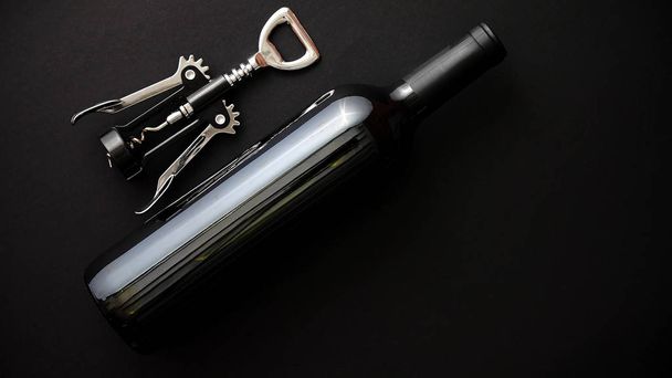 Red wine bottle and corkscrew on black matte background. - Fotoğraf, Görsel
