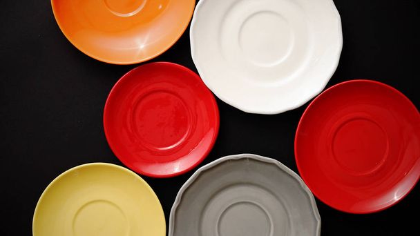Colorful empty plates and saucers over black background. - Photo, Image