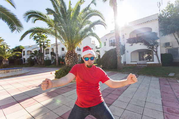 Διακοπές και οι άνθρωποι έννοια - αστείος άνθρωπος στον χριστουγεννιάτικο καπέλο χορό σε εξωτερικούς χώρους. - Φωτογραφία, εικόνα