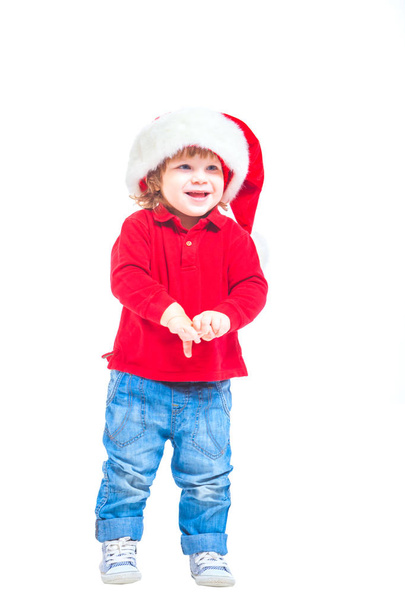 Christmas. A little boy in a Santa hat, in a red jacket and blue jeans. Isolated on white background. - Photo, Image