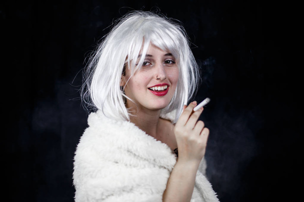 Attractive young woman in costume smoking cigar and looking at camera while standing on black background  - Photo, Image