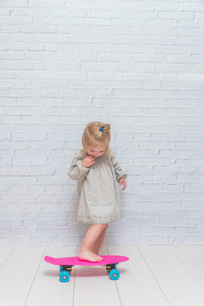 the girl, child on a skateboard on a white brick wall background - Zdjęcie, obraz