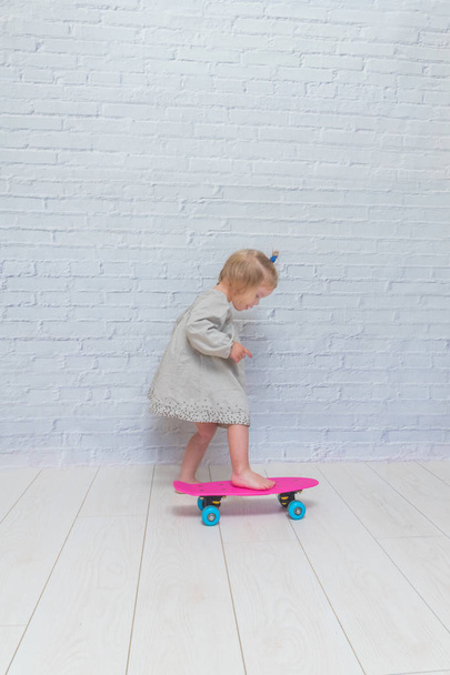 the girl, child on a skateboard on a white brick wall background - Photo, image
