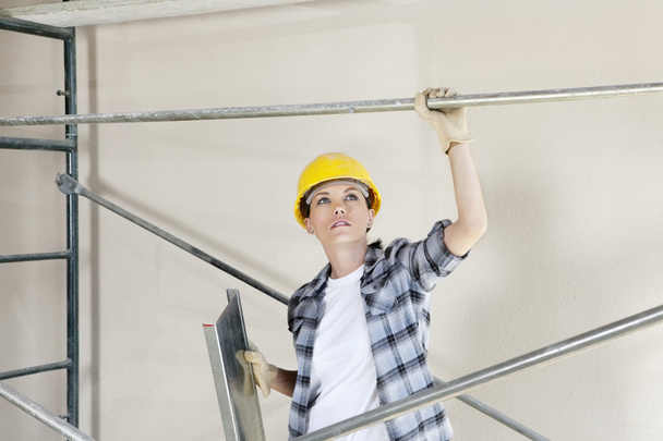 Mid adult female architect looking up while standing under scaffold at construction site - 写真・画像