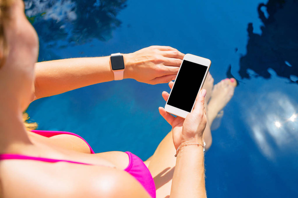 Mujer usando smartwatch y teléfono móvil junto a la piscina
 - Foto, imagen