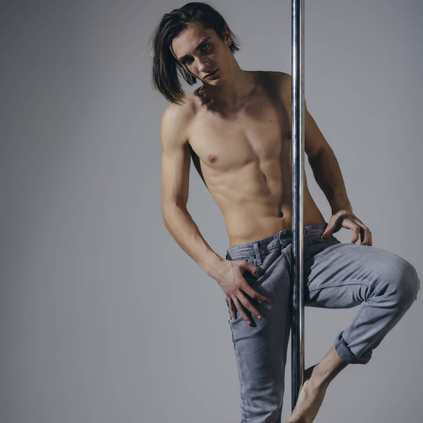 Charming man pole dancer with pylon in the studio on the grey background. he is using the pylon like a fulcrum, copy space - Fotografie, Obrázek
