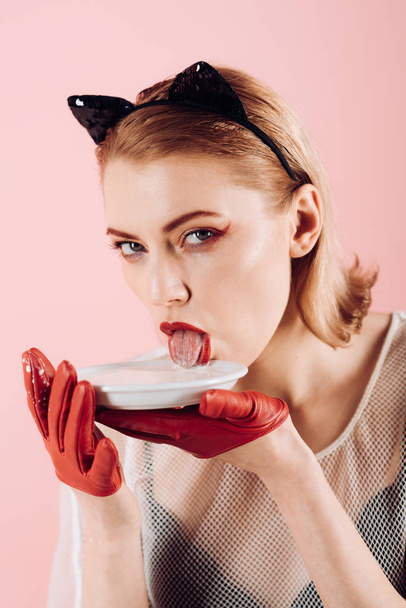 Dziewczyna w uszach kotek i czerwone rękawice z jogurtem na różowym tle. Diety i zdrowia. Kot sexy kobieta lizać mleka z płytki. Jedzenie i picie. Ekologia produktu i heath. Kobieta Kot jeść kwaśnej śmietany. - Zdjęcie, obraz