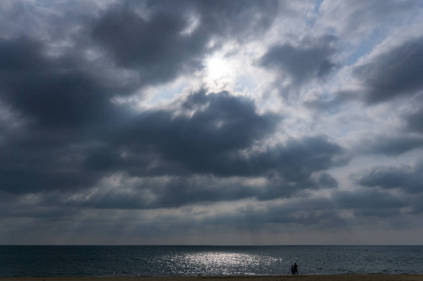 Ακτίνα φωτός που διαπερνά το cloud με την άκαμπτη φυσική του ομορφιά, γραφική μεγαλείο έδειχνε μπροστά μου. Ένα ζευγάρι ήταν βυθισμένο στη φυσική, casual περιπάτους βρόχο aroud στην παραλία. Παραλία Nai Yang είναι ένα απομακρυσμένο μέρος στο Πουκέτ. - Φωτογραφία, εικόνα