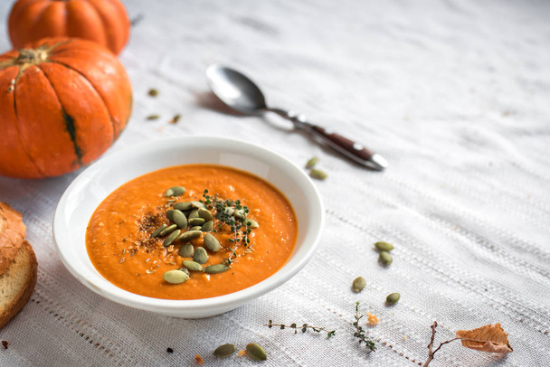 Pumpkin soup and organic pumpkins, top view. Seasonal autumn food - Spicy pumpkin soup with herbs and seeds. - Фото, изображение