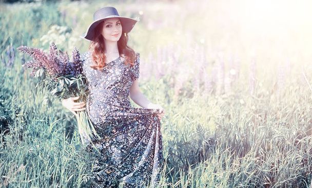 Pregnant girl in a field with lupines in a dress - Photo, Image