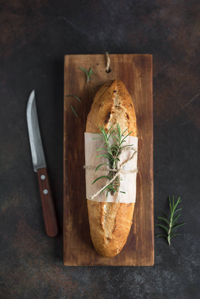 Čerstvý domácí chléb s rozmarýnem na rustikální dřevěné pozadí, pohled shora, kopie prostoru. Kváskový chléb mini bageta. - Fotografie, Obrázek
