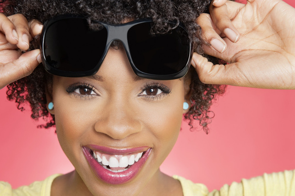 Portrait of a cheerful African American woman holding sunglasses over colored background - Fotografie, Obrázek