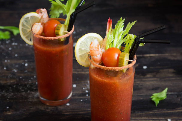 Bloody Mary Cocktail in glasses with garnishes. Tomato Bloody Mary spicy drink on dark wooden background with copy space. - Φωτογραφία, εικόνα