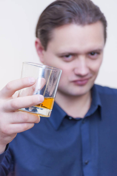 Portret młodego człowieka rasy kaukaskiej, z niebieską koszulę Wyświetlono oferty szklankę whisky, brandy, na białym tle. - Zdjęcie, obraz