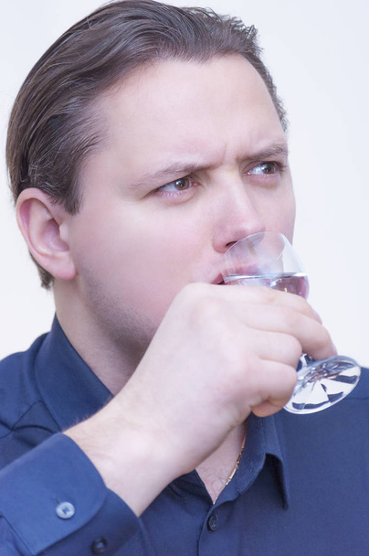 Portrait of young Caucasian Ethnicity man with blue shirt drinking Vodka from glass shot on white background. - Foto, immagini